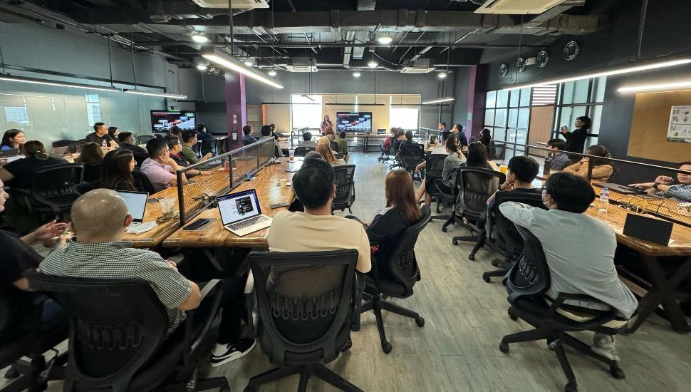 2X workers at desks with laptops in a meeting.