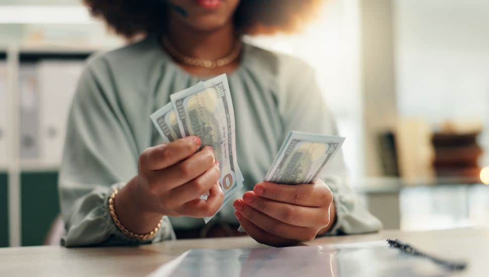 Black woman county $100 bills in her hands.